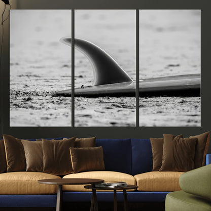 A black and white close-up of a surfboard fin resting on the sandy shore, highlighting minimalist beach aesthetics and classic surf culture.