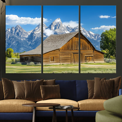 A rustic wooden barn sits in front of towering mountain peaks under a clear blue sky, perfect for farmhouse or cabin style interiors.