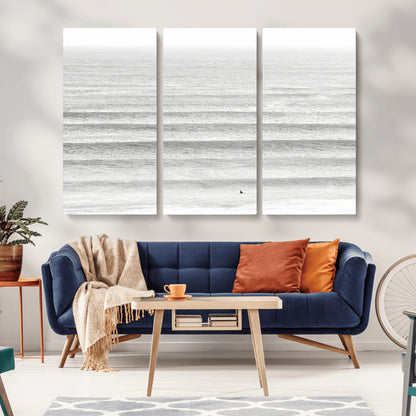 Monochrome photo of a lone surfer in calm layered waves, perfect for minimalist coastal or moody ocean-inspired wall decoration.