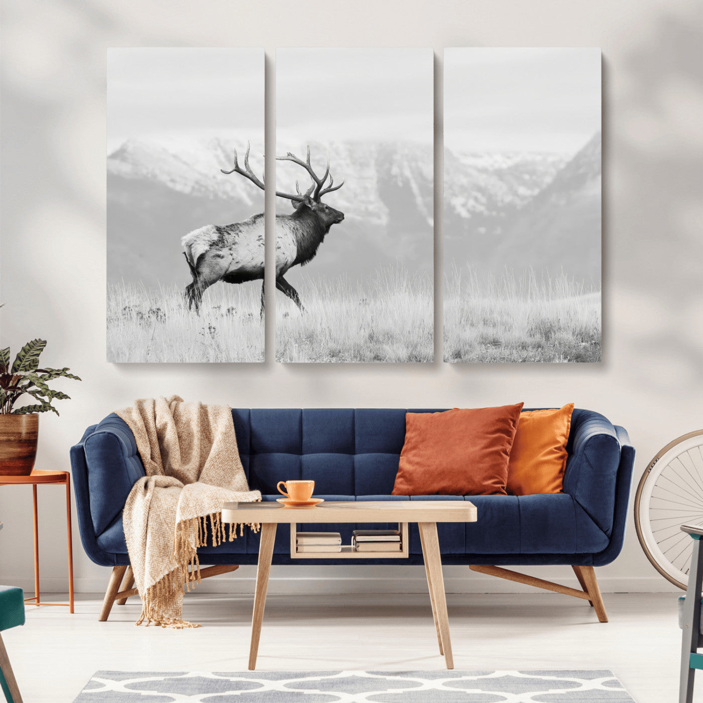 Black and white photograph of a majestic elk standing in a grassy field with snow-capped mountains in the background, creating a bold and rustic wilderness scene.