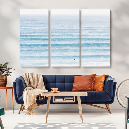 Minimalist ocean view with soft blue waves and a lone surfer, creating a serene and airy coastal aesthetic, perfect for tranquil home decor.