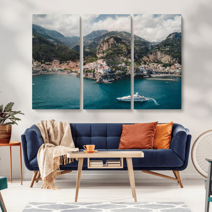 Aerial view of Amalfi Coast, Italy, with colorful hillside houses, lush green mountains, and a luxury yacht sailing in turquoise waters.