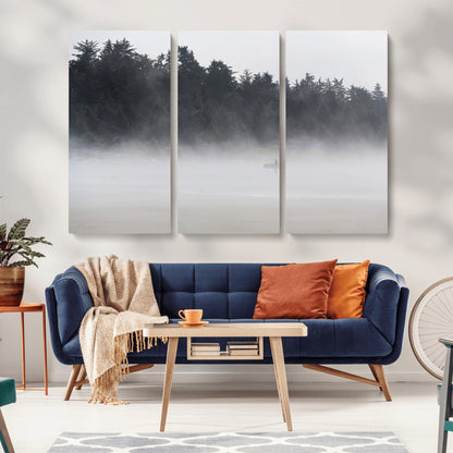 A lone surfer carrying a board through a misty shoreline, surrounded by dense trees and fog, creating a peaceful and mysterious coastal scene.