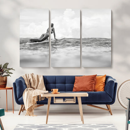 A black and white ocean scene featuring a surfer girl waiting on her board, gazing at the horizon, capturing a tranquil and adventurous coastal moment.