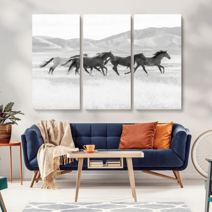 A black and white image of wild horses running freely across an open grassland, capturing the power and beauty of untamed nature in a rustic western setting.