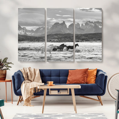 A black and white landscape of wild horses grazing in a vast grassland with towering mountains in the background, creating a moody and rustic western aesthetic.