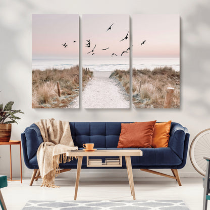A peaceful coastal pathway leading to the ocean, with birds flying across a soft pastel sky, creating a calm and scenic beach atmosphere.