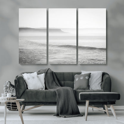 A black and white minimalist seascape featuring soft rolling waves and misty distant cliffs, creating a serene and timeless coastal atmosphere.