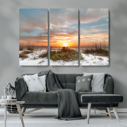 A tranquil beach scene featuring golden sunset hues over the water, with grasses in the foreground and a peaceful, serene atmosphere.