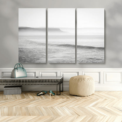 A black and white minimalist seascape featuring soft rolling waves and misty distant cliffs, creating a serene and timeless coastal atmosphere.