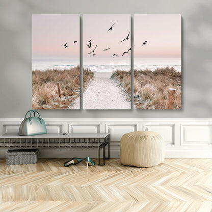 A peaceful coastal pathway leading to the ocean, with birds flying across a soft pastel sky, creating a calm and scenic beach atmosphere.