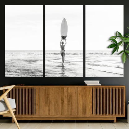 Black and white image of a female surfer holding a surfboard above her head while walking toward the ocean, creating a minimalist and bold coastal aesthetic.