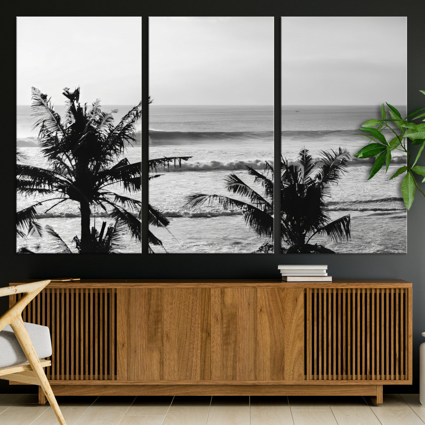 Black and white view of ocean waves crashing on a tropical coastline, framed by silhouetted palm trees under a vast, open sky.