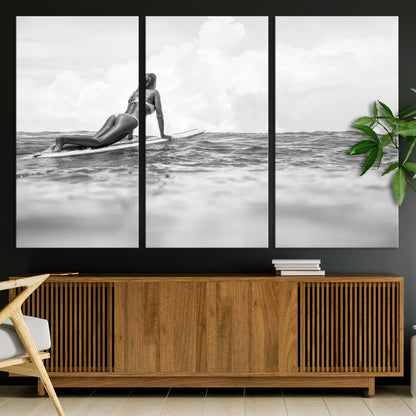 A black and white ocean scene featuring a surfer girl waiting on her board, gazing at the horizon, capturing a tranquil and adventurous coastal moment.