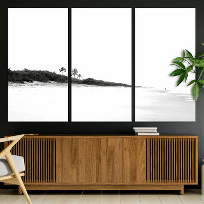A black and white minimalist coastal scene with a vast open beach, distant palm trees, and a lone figure walking along the shoreline, evoking serenity and solitude.