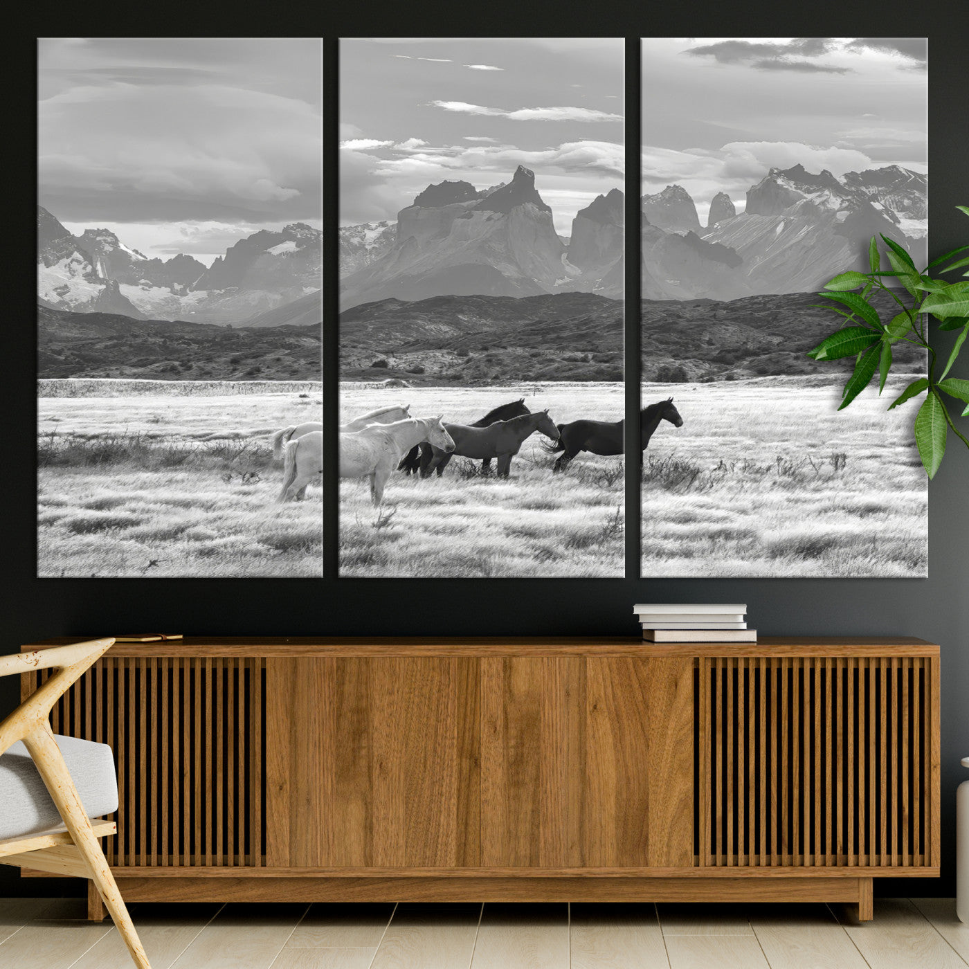 A black and white landscape of wild horses grazing in a vast grassland with towering mountains in the background, creating a moody and rustic western aesthetic.