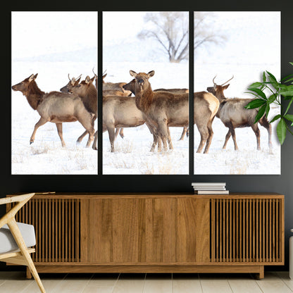 A group of elk standing on snowy terrain with a tree in the background, perfect for rustic or lodge-style winter wall decor.