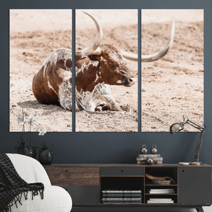 Texas Longhorn bull resting on dusty ground with warm tones, ideal for rustic western or farmhouse-themed wall decor.