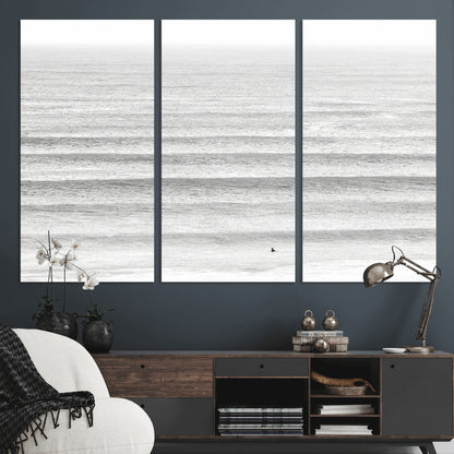 Monochrome photo of a lone surfer in calm layered waves, perfect for minimalist coastal or moody ocean-inspired wall decoration.