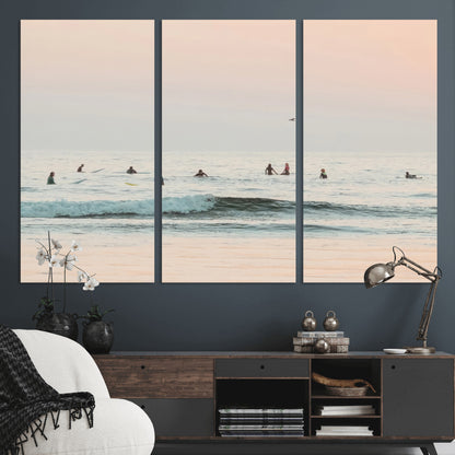 Dreamy photo of surfers waiting on soft pastel waves under a pink sunset sky, ideal for soft coastal minimalist or serene ocean-themed home decor.