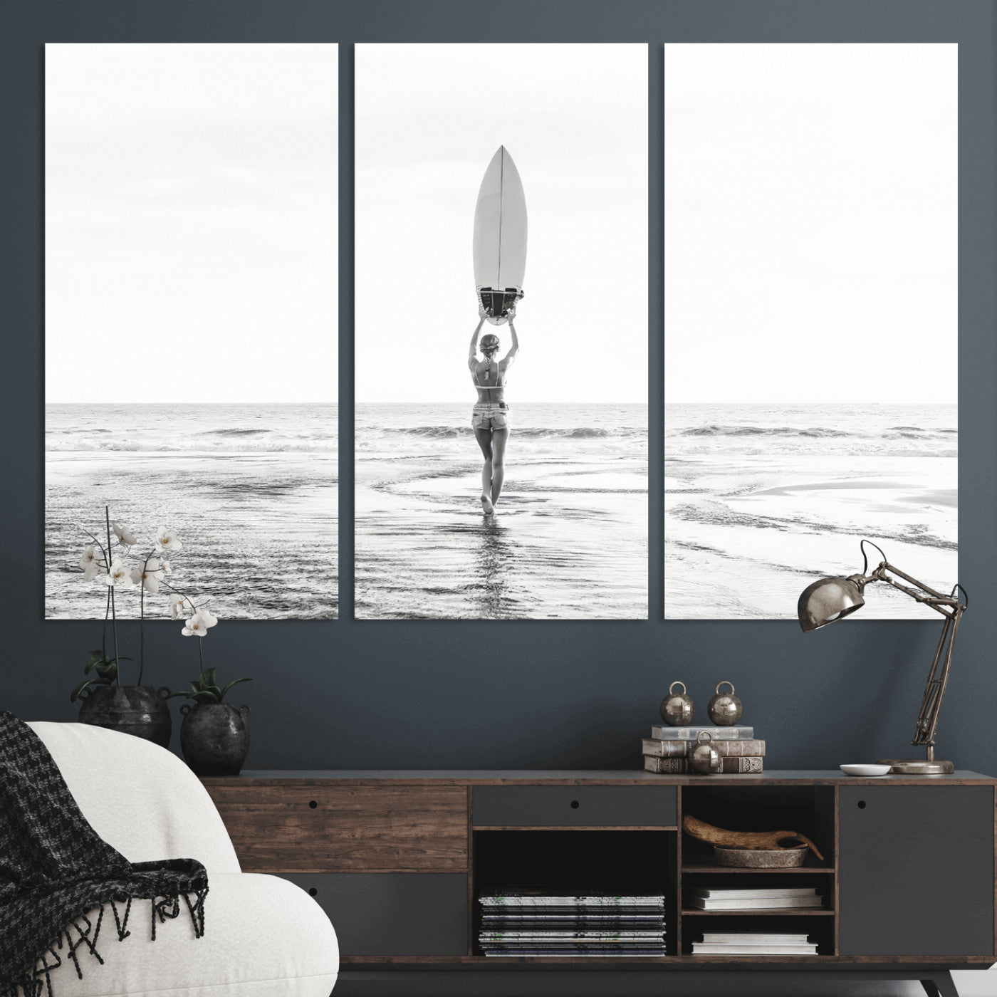 Black and white image of a female surfer holding a surfboard above her head while walking toward the ocean, creating a minimalist and bold coastal aesthetic.