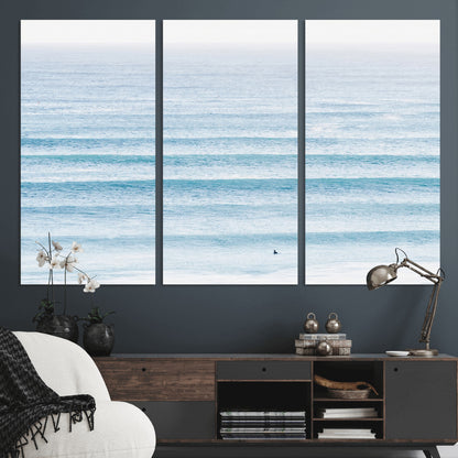 Minimalist ocean view with soft blue waves and a lone surfer, creating a serene and airy coastal aesthetic, perfect for tranquil home decor.