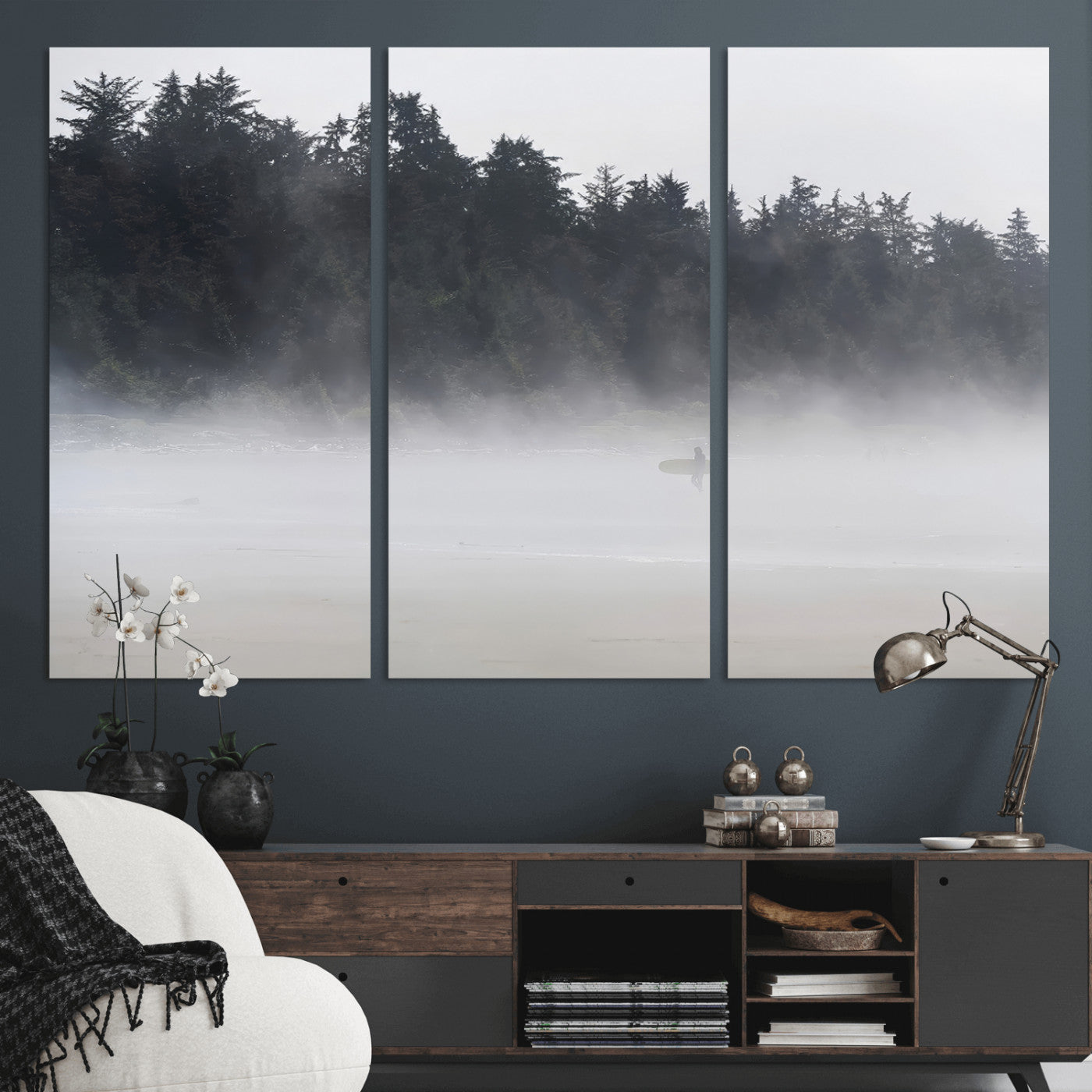 A lone surfer carrying a board through a misty shoreline, surrounded by dense trees and fog, creating a peaceful and mysterious coastal scene.
