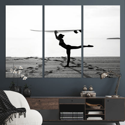 A woman balances a surfboard on her head while striking a yoga pose on the beach, silhouetted against a calm ocean horizon.
