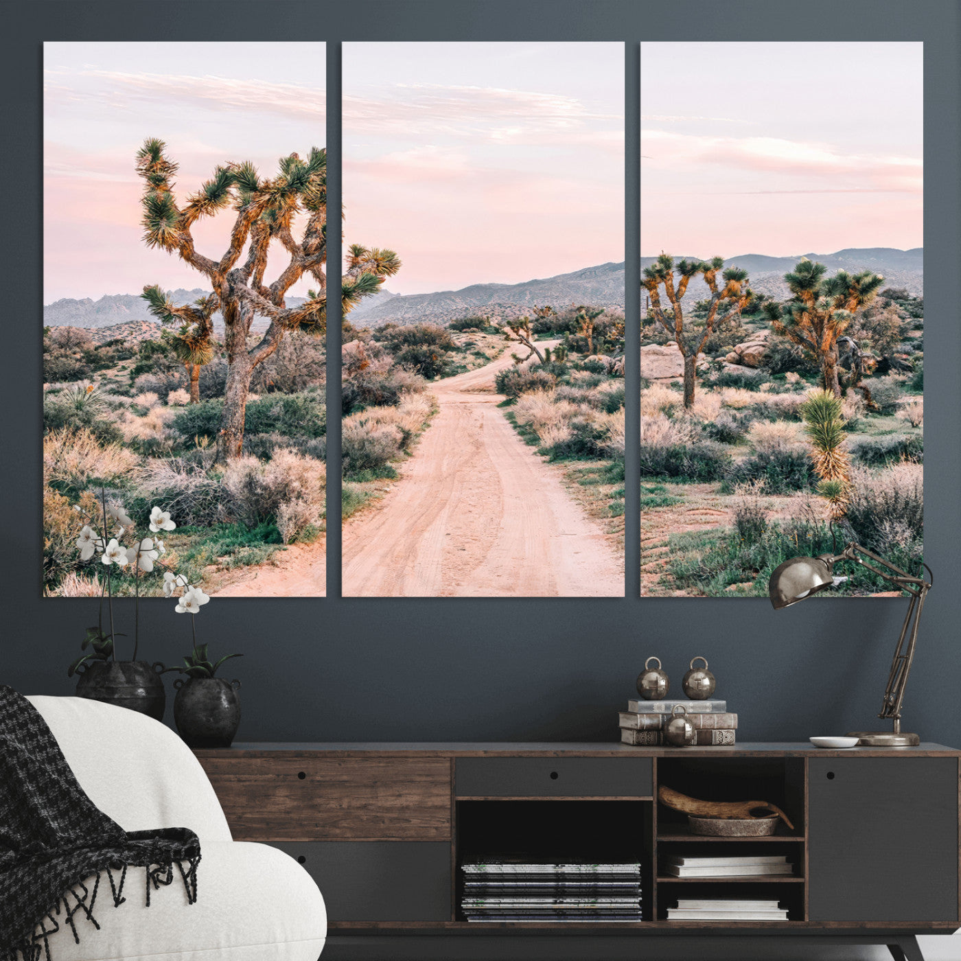 A dusty road winding through Joshua Tree National Park, framed by iconic twisted trees and warm desert tones under a soft pastel sky.