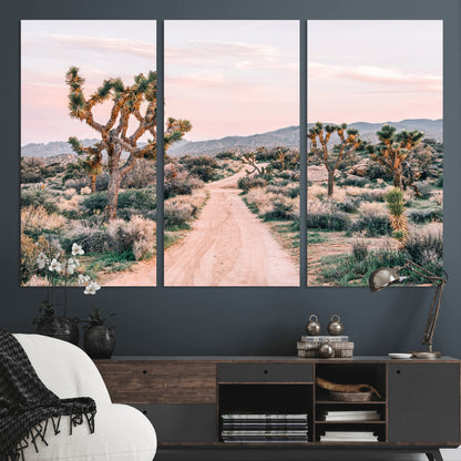 A dusty road winding through Joshua Tree National Park, framed by iconic twisted trees and warm desert tones under a soft pastel sky.