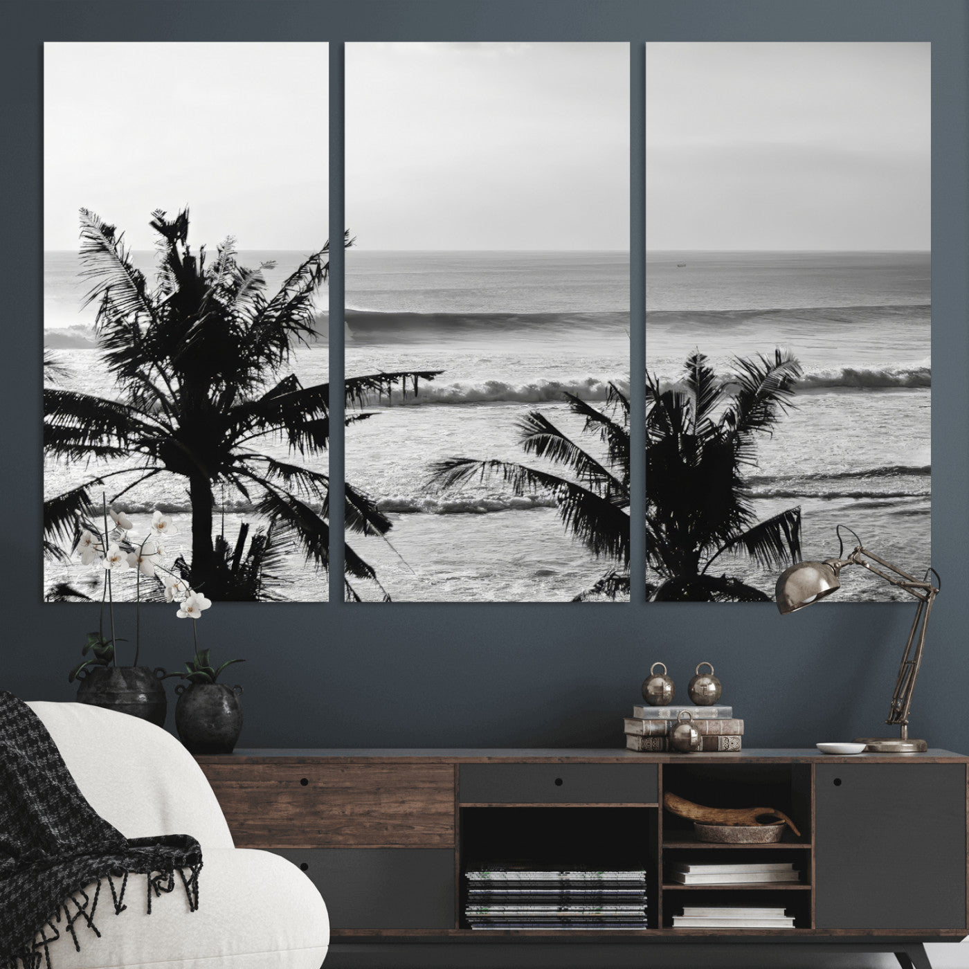 Black and white view of ocean waves crashing on a tropical coastline, framed by silhouetted palm trees under a vast, open sky.