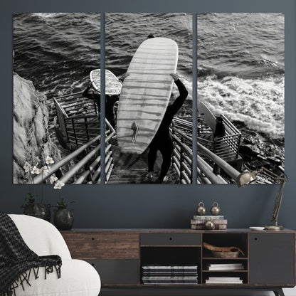Black and white photo of surfers carrying boards down a rugged cliffside stairway, capturing a bold and adventurous coastal scene.