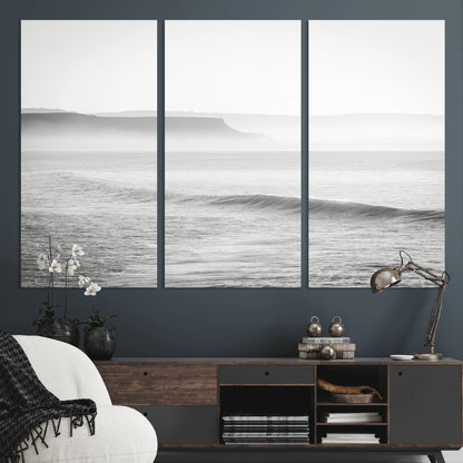 A black and white minimalist seascape featuring soft rolling waves and misty distant cliffs, creating a serene and timeless coastal atmosphere.