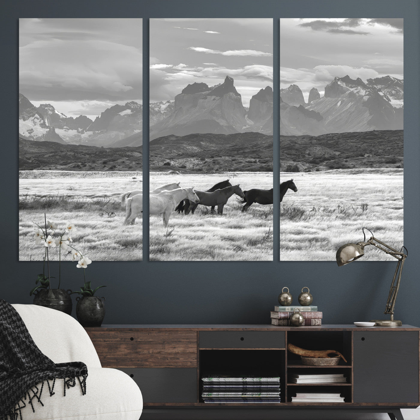 A black and white landscape of wild horses grazing in a vast grassland with towering mountains in the background, creating a moody and rustic western aesthetic.