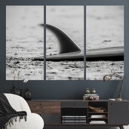 A black and white close-up of a surfboard fin resting on the sandy shore, highlighting minimalist beach aesthetics and classic surf culture.