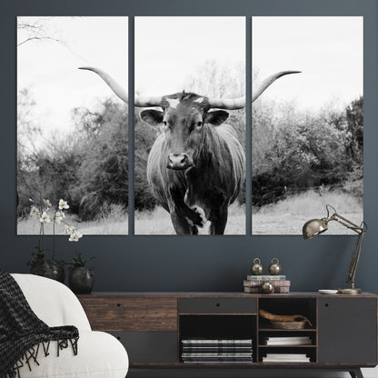 Black and white photo of a longhorn cow in a field, perfect for rustic farmhouse or western-themed interior wall decoration.