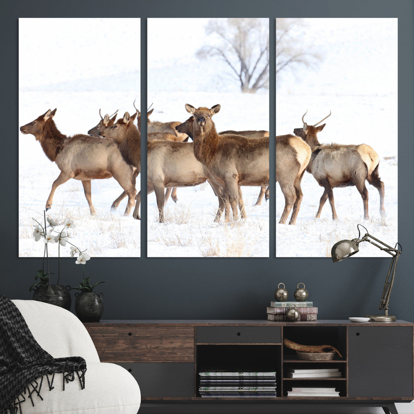 A group of elk standing on snowy terrain with a tree in the background, perfect for rustic or lodge-style winter wall decor.