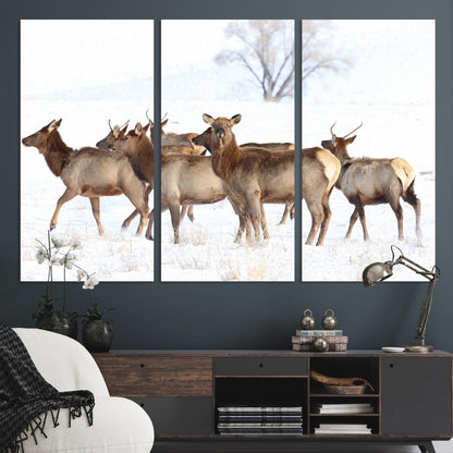 A group of elk standing on snowy terrain with a tree in the background, perfect for rustic or lodge-style winter wall decor.