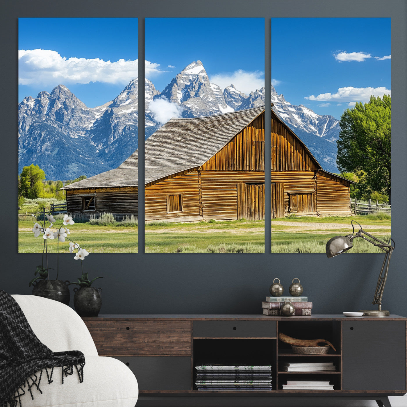 A rustic wooden barn sits in front of towering mountain peaks under a clear blue sky, perfect for farmhouse or cabin style interiors.