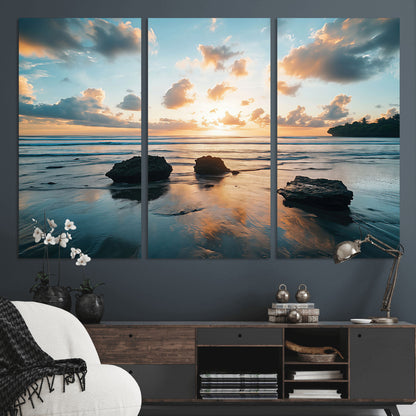 A serene beach at sunset with vibrant clouds, calm water, and rocks in the foreground reflecting the warm colors of the setting sun.
