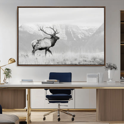 Black and white photograph of a majestic elk standing in a grassy field with snow-capped mountains in the background, creating a bold and rustic wilderness scene.