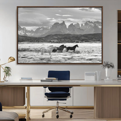 A black and white landscape of wild horses grazing in a vast grassland with towering mountains in the background, creating a moody and rustic western aesthetic.