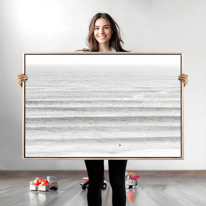 Monochrome photo of a lone surfer in calm layered waves, perfect for minimalist coastal or moody ocean-inspired wall decoration.