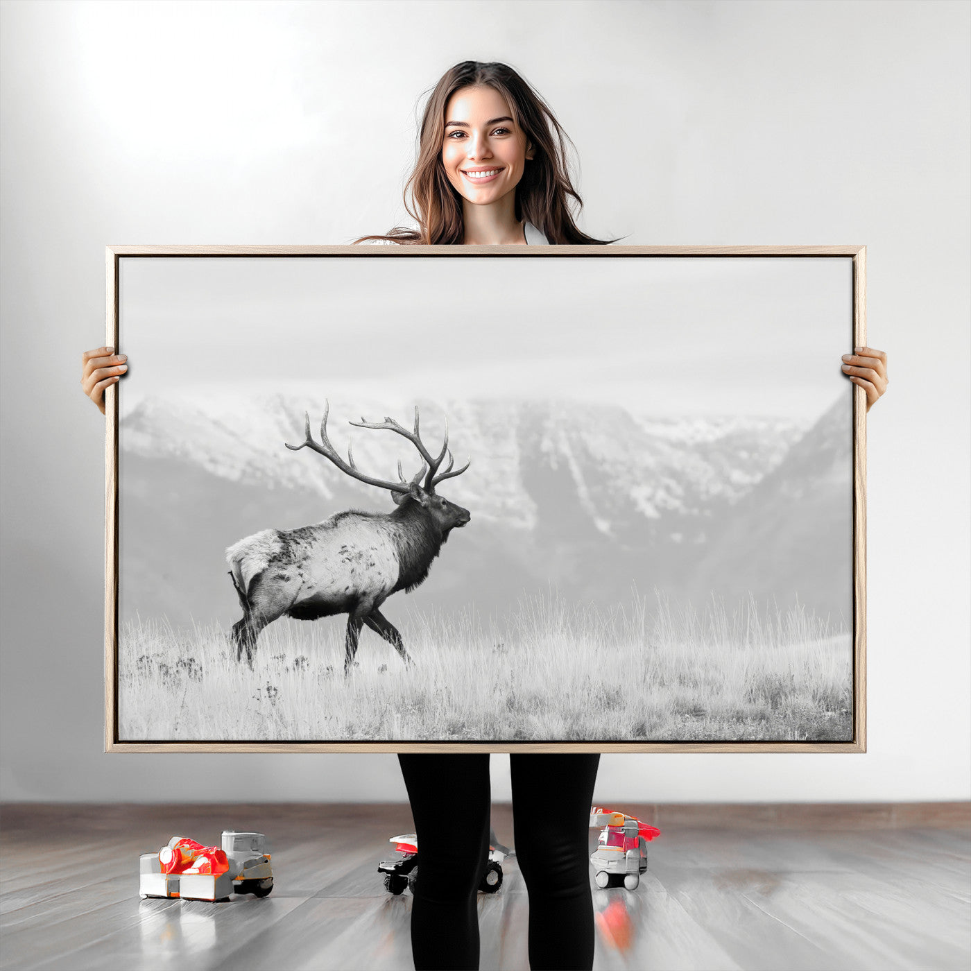 Black and white photograph of a majestic elk standing in a grassy field with snow-capped mountains in the background, creating a bold and rustic wilderness scene.
