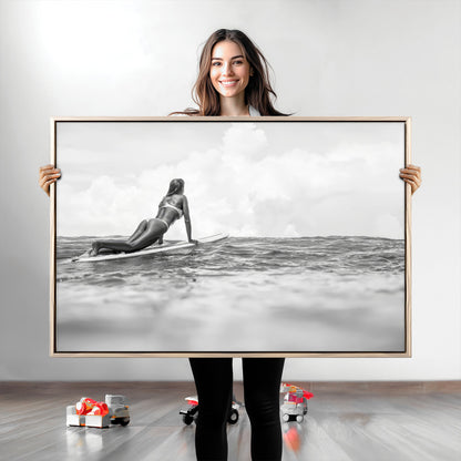 A black and white ocean scene featuring a surfer girl waiting on her board, gazing at the horizon, capturing a tranquil and adventurous coastal moment.