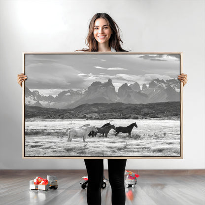 A black and white landscape of wild horses grazing in a vast grassland with towering mountains in the background, creating a moody and rustic western aesthetic.