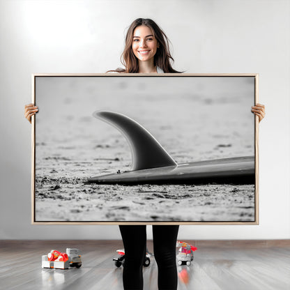 A black and white close-up of a surfboard fin resting on the sandy shore, highlighting minimalist beach aesthetics and classic surf culture.