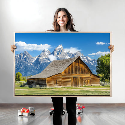 A rustic wooden barn sits in front of towering mountain peaks under a clear blue sky, perfect for farmhouse or cabin style interiors.
