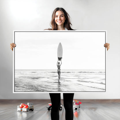 Black and white image of a female surfer holding a surfboard above her head while walking toward the ocean, creating a minimalist and bold coastal aesthetic.