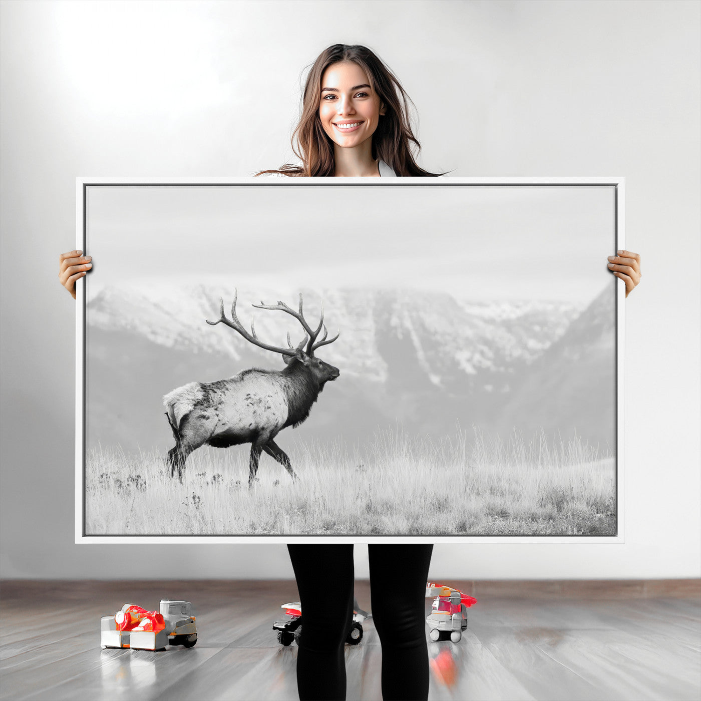 Black and white photograph of a majestic elk standing in a grassy field with snow-capped mountains in the background, creating a bold and rustic wilderness scene.